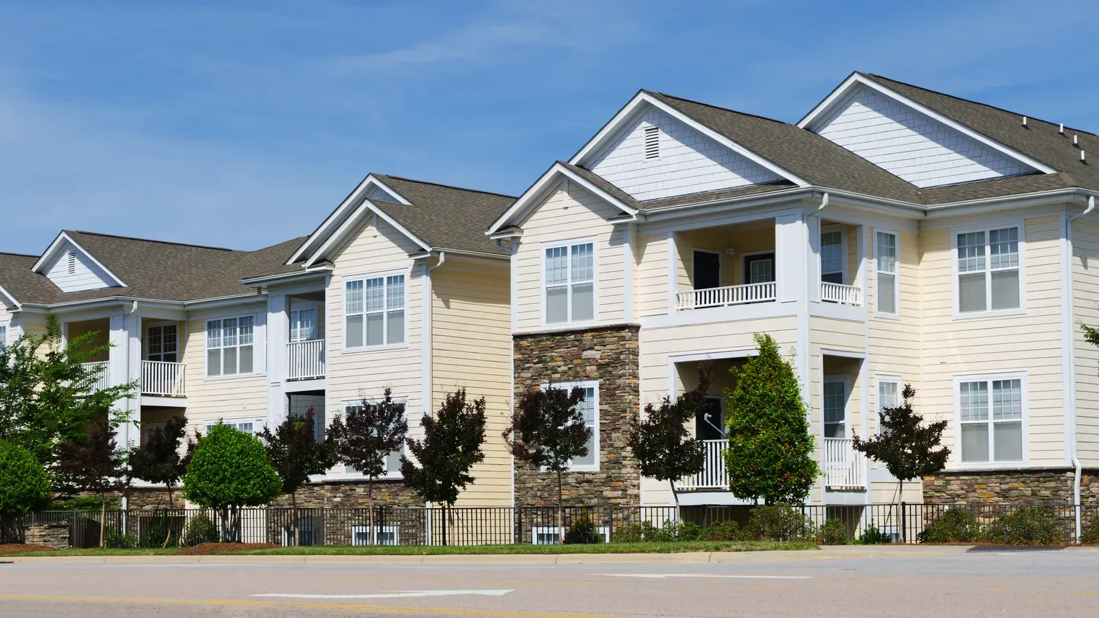 A professional contractor installing new asphalt shingles on a multifamily building's roof, while also replacing the vinyl siding. | You First Home Services