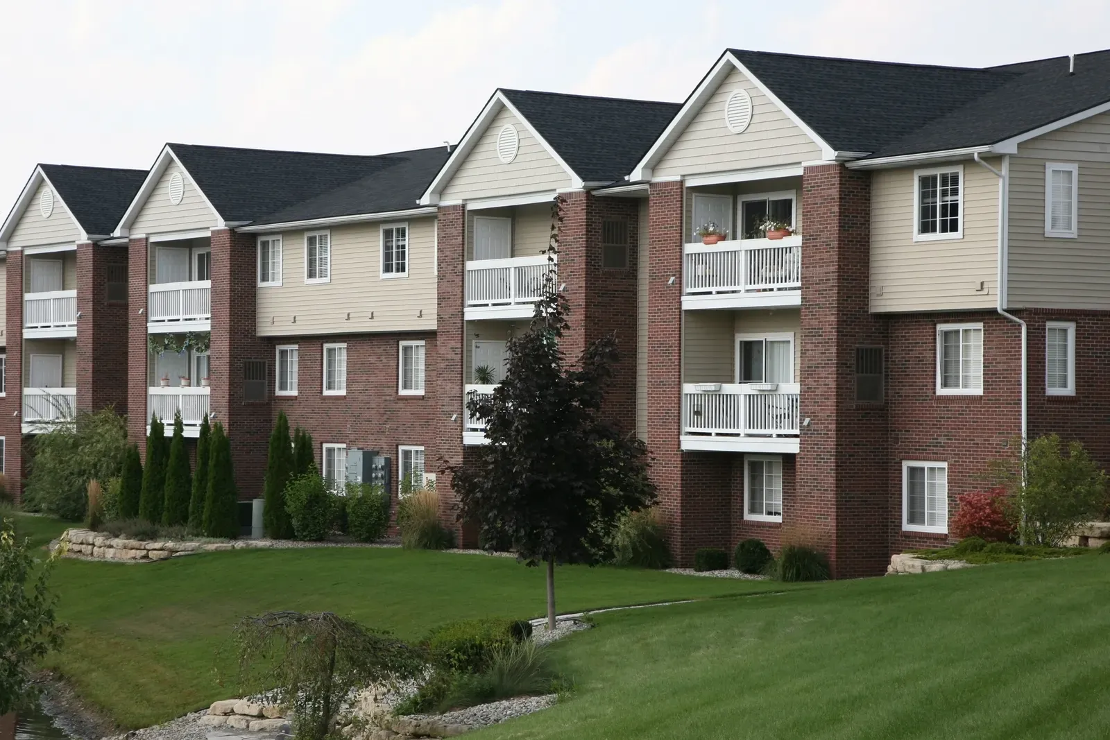 A photo of a multistory building with a new asphalt roof being installed and a window being replaced, with another window showing a picture inside. | You First Home Services